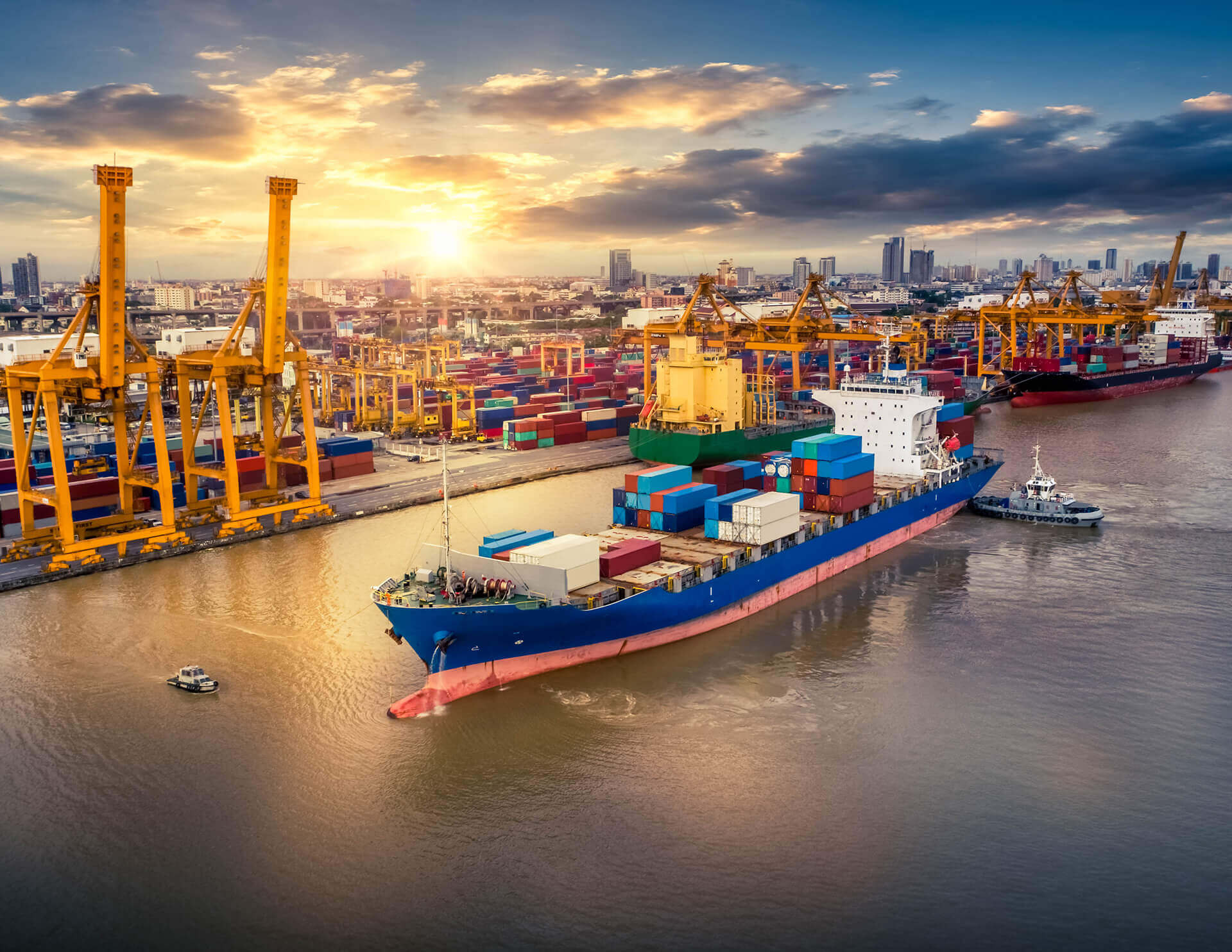 Container ship berthed at a busy port with quay cranes at sunset